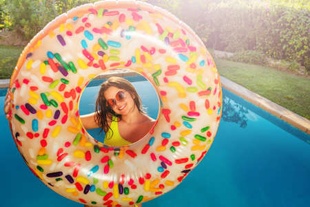 Happy smiling teen girl stand with inflatable buoy doughnut on the border of swimming poolの写真素材