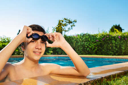 Happy handsome boy on the border of swimming pool hold in hands swim gogles and smileの写真素材