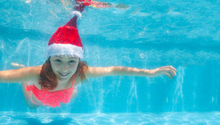Happy girl dive and swim underwater wearing Santa Claus hat in the pool smile on her Christmas vacationの写真素材