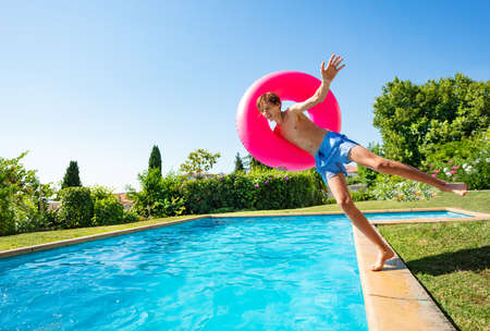 Happy handsome boy with inflatable red buoy jump into swimming pool view from sideの写真素材