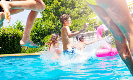 Boy in a group of friends jump into water pool together splashing downの写真素材
