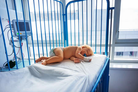 Little one year old toddler sleep in hospital after operation with catheter in his hand and pacifierの写真素材
