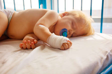 Close photo of a small toddler sleep in hospital with catheter in his hand and pacifier