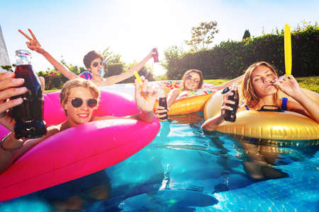 Many happy children party, drink cola and blow noisemakers in swimming pool