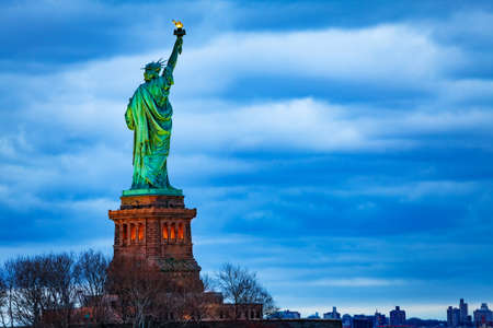 The Statue of Liberty over the New York cityscape from Black Tom Island at evening duskの写真素材