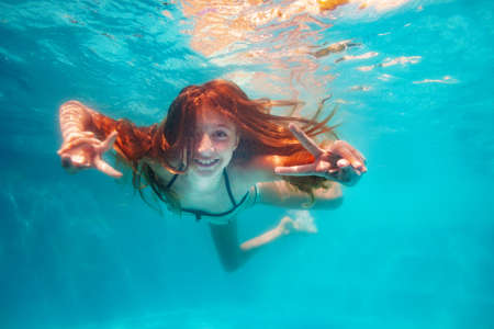 Nice friendly smiling happy portrait of the girl swim underwater in the pool and showing v victory gesture with handsの写真素材