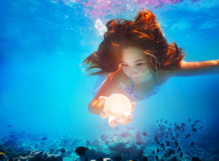 Portrait of a girl swim under water with magic shining ball sphere in her hand beautiful mixed media conceptの写真素材