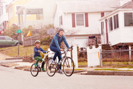 Family bike portrait with little happy boy ride on a tow tandem bicycle attached to father on urban street side view