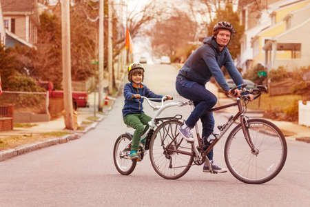 Family bike portrait with little happy boy ride on a tow tandem bicycle attached to father on urban streetの写真素材