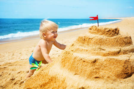 Handsome little toddler play build sand castle on the beach near the seaの写真素材