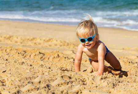 Happy little toddler boy crawl on the beach wearing children protective sunglassesの写真素材