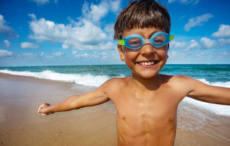 Close portrait of young boy in swimming googles stand on the beachの写真素材