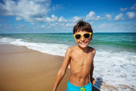 Portrait of a happy boy stand on the beach near the sea wear sunglasses and smileの写真素材