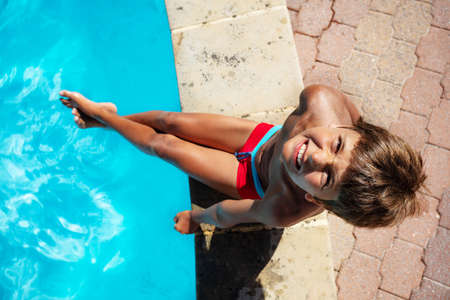 Photo of the ten years old boy sit on the side of the border of the swimming poolの写真素材