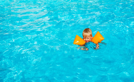 Cute little toddler boy swim wearing inflatable shoulder straps in the swimming poolの写真素材