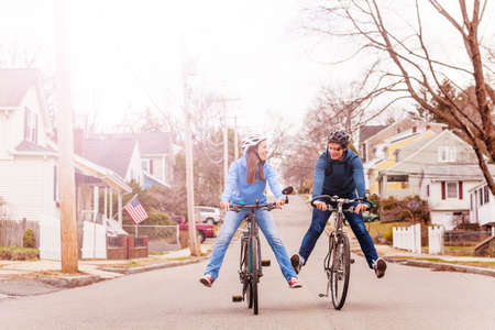 Young couple ride a bicycle fun lifting legs smile on urban American streetの写真素材