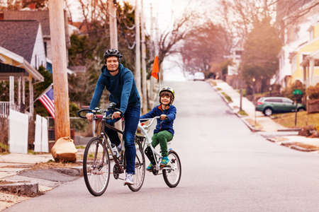 Little happy boy ride on a tow tandem bike with flag attached to father on urban streetの写真素材