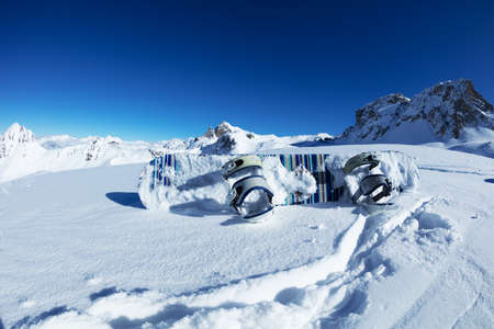 Photo of child snowboard lay in the snow on top of the mountains over blue sky on sunny day on ski resortの写真素材