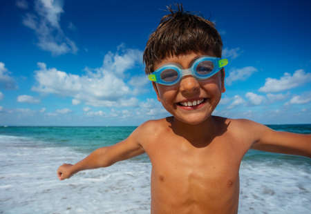Close portrait of small boy in swimming googles stand on the beachの写真素材