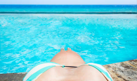 Photo of a belly a pregnant woman near the swimming pool with sea view
