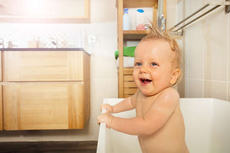 Little toddler boy stand in the bathtub and smile