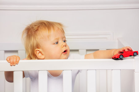 Blond baby boy play with red car in the cribの写真素材