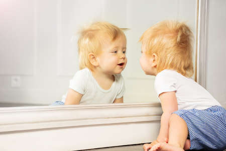Close portrait of blond toddler boy look in mirrorの写真素材