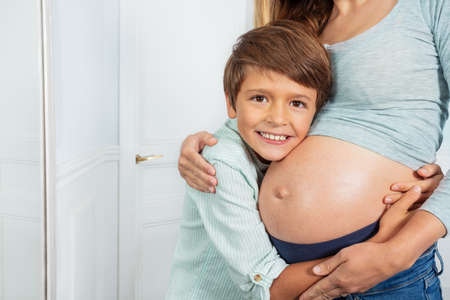 Happy ten years old son hug moms pregnant bellyの写真素材