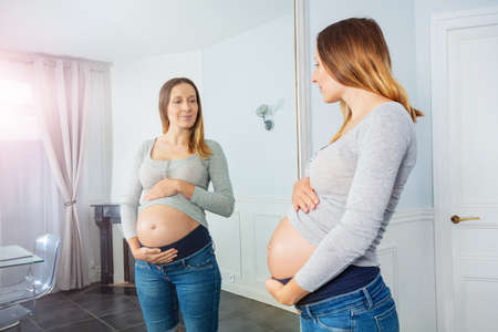 Happy pregnancy woman posing before mirror at homeの写真素材