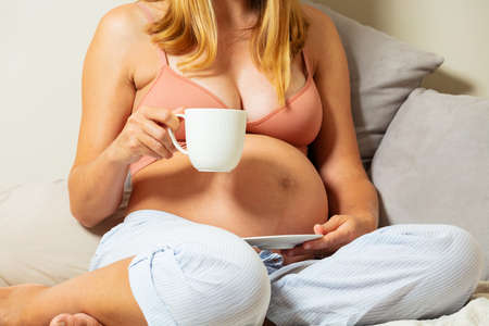 Close photo of a pregnant woman sit with tea cupの写真素材
