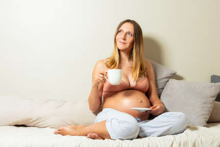 Relaxed happy pregnant woman sit with tea cupの写真素材