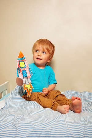 Baby boy play with paper rocket sitting on the bedの写真素材
