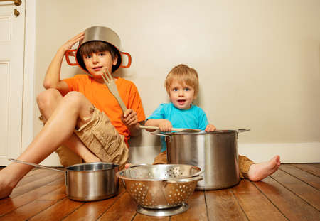 Two kids, boys play with kitchenware pans at homeの写真素材