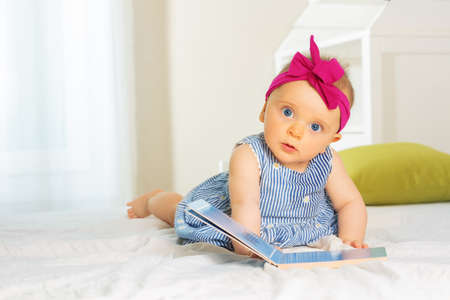 Little stylish baby girl leaf through book in bedの写真素材