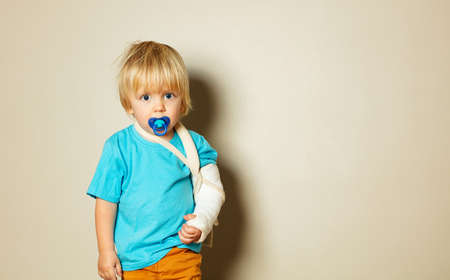 Sad boy with pacifier and broken hand in plasterの写真素材