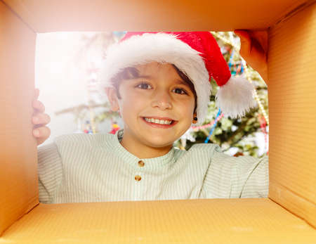 Smiling boy in Santa hat looks inside present boxの写真素材