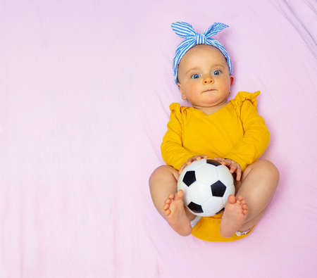 Beautiful baby girl lay with football ball in bedの写真素材