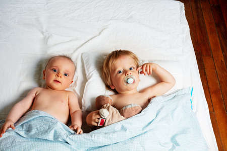 Little babies, boy and girl lay in a bed waking upの写真素材
