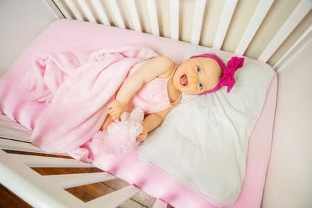 Baby girl lay in crib bed laugh and look upの写真素材