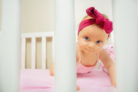 Baby girl stand on hands in the bed wear pink bowの写真素材
