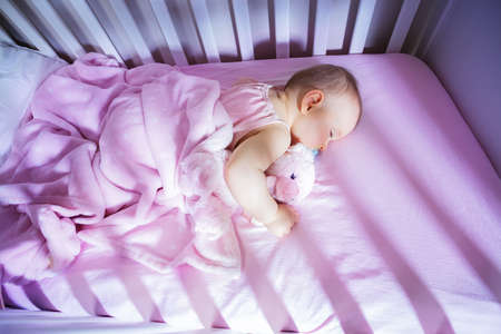 Little baby girl sleep in crib hugging pink bearの写真素材