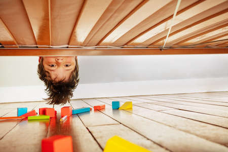 Funny portrait of a boy look down under the bedの写真素材