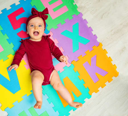 Cute little baby girl with red bow on ABC carpetの写真素材