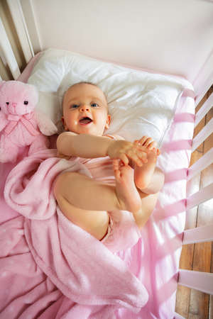 Baby girl lay in pink bed touching legs laughingの写真素材