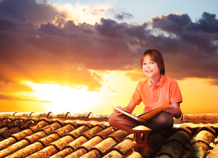 Boy sit on a roof and read book, view over sunsetの写真素材