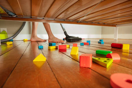Feet of boy clean floor with mess under the bedの写真素材