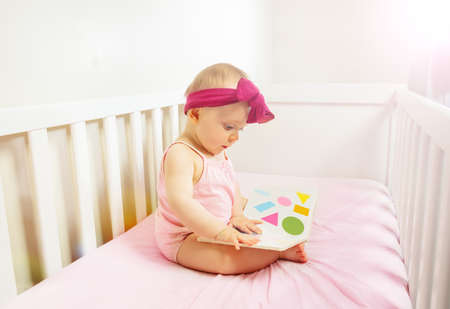Baby sit in crib bed look at the book with shapesの写真素材