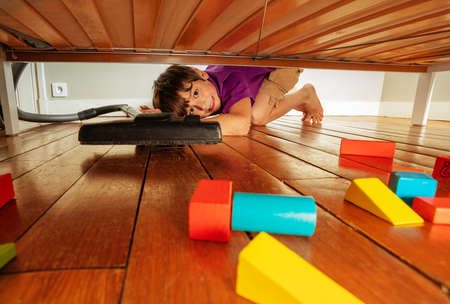 Boy vacuum clean under the bed full of toy blocksの写真素材