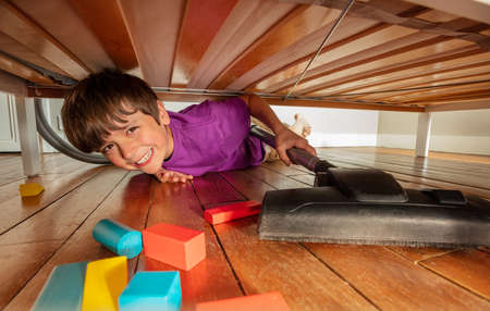 Boy under the bed clean floor with vacuum cleanerの写真素材