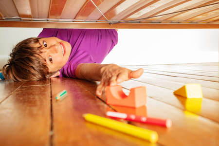 Boy stretch to reach color toy block under the bedの写真素材